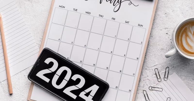 Foto de calendário de mesa em prancheta com um celular exibindo o número 2024 sobre ele, xícara de café e clipes ao redor