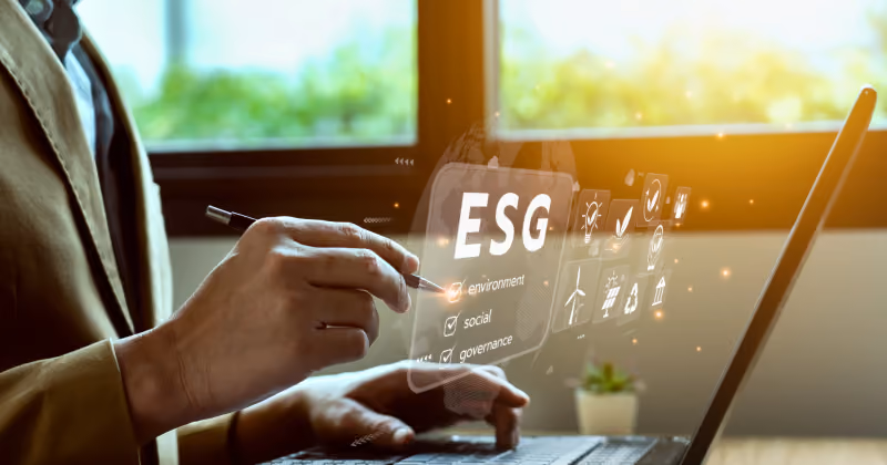 Foto de mãos em um laptop tocando painel holográfico com a sigla ESG e os rótulos environment, social e governance
