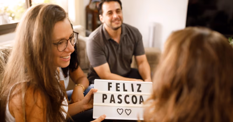 Foto de três pessoas conversando numa sala, uma delas segurando um quadro luminoso com os dizeres Feliz Páscoa e dois corações
