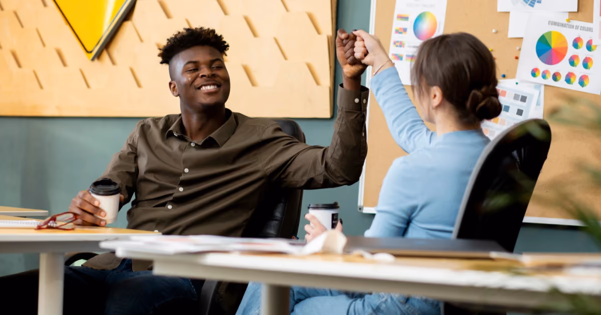 Foto de dois colegas comemorando com as mãos unidas sobre a mesa do escritório, com gráficos coloridos ao fundo