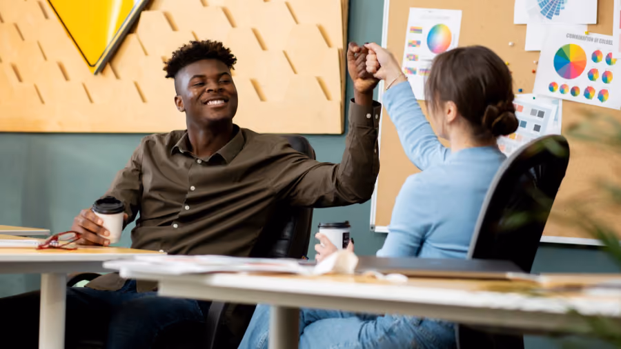 Foto de dois colegas comemorando com as mãos unidas sobre a mesa do escritório, com gráficos coloridos ao fundo